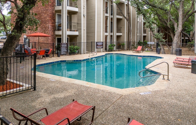 A small pool surrounded by a black fence and red sunshades.