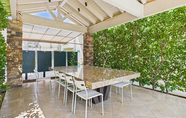 A patio with a table and chairs is surrounded by greenery.