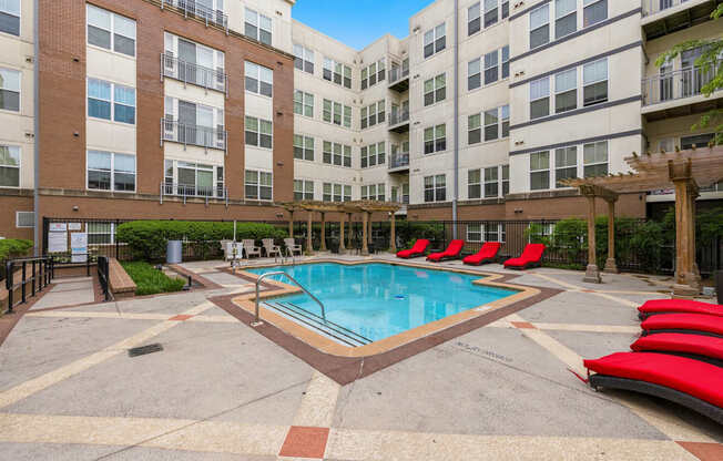A swimming pool surrounded by red lounge chairs and apartment buildings.