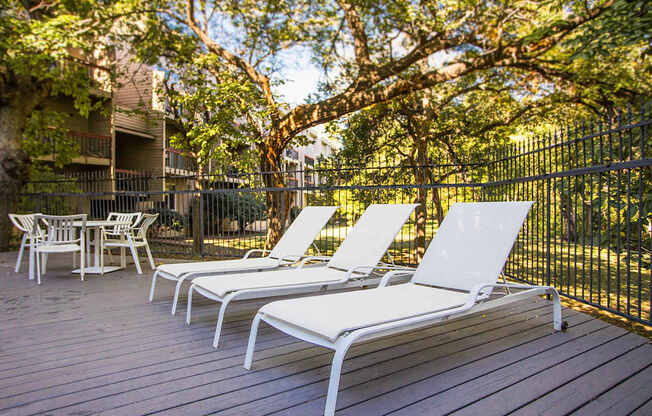 three lounge chairs on a deck in front of a fence and trees