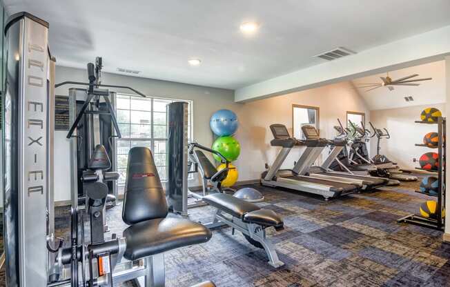 Fitness center with exercise equipment, large window, and ceiling fan.