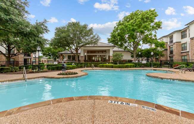 A pool surrounded by trees and a building in the background.