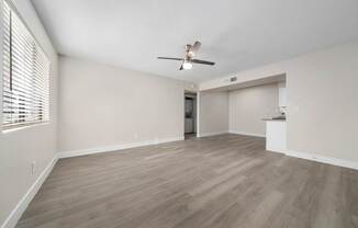 A room with a ceiling fan and light, wooden floors, and a doorway leading to another room.