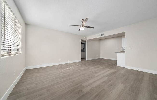 A room with a ceiling fan and light, wooden floors, and a doorway leading to another room.