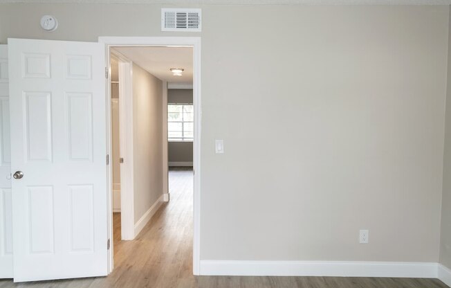 an empty room with a white door and a hallway to a bedroom