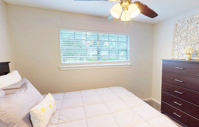 A bedroom with a bed, dresser, and window with blinds.