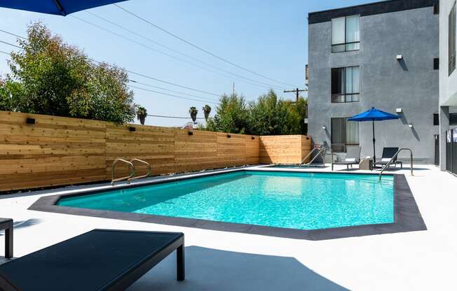 a pool in a backyard with a wooden fence and a gray building in the background