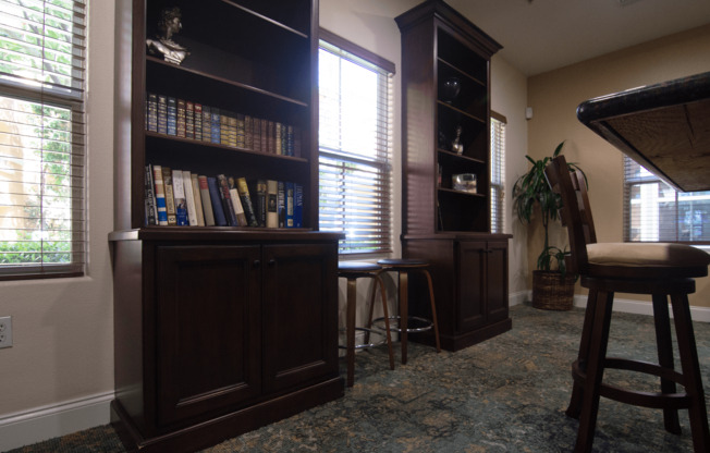 A room with a bookcase, a bar stool, and a potted plant.