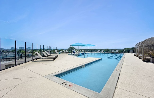 A large outdoor swimming pool with sun loungers and a clear blue sky.