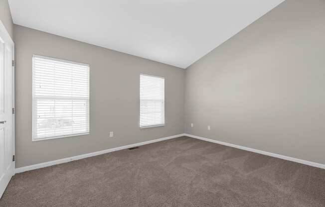 an empty living room with carpet and two windows at Traditions at Slate Ridge, Reynoldsburg, OH