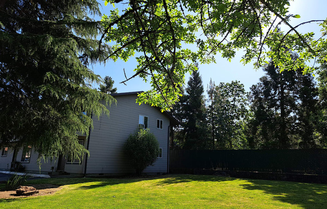 a backyard with a white house and trees with green grass