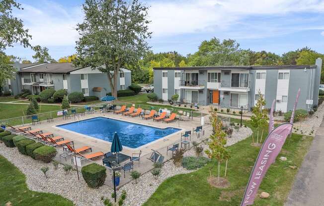 A pool surrounded by chairs and trees with apartment buildings in the background.
