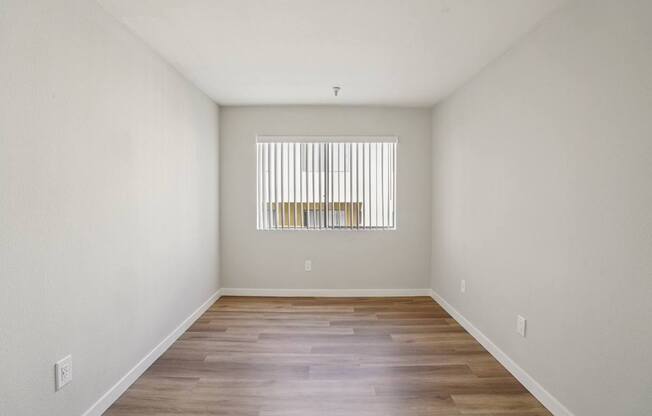 A room with wooden floors and a window with blinds.