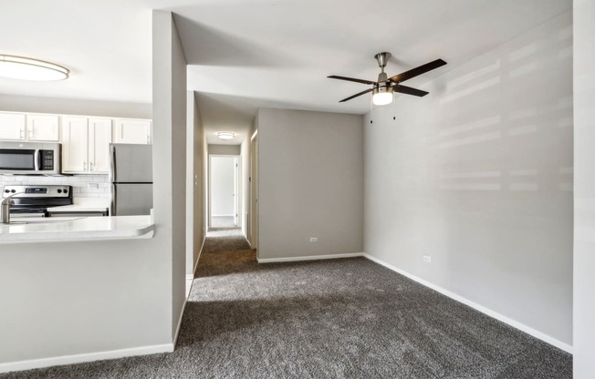 an empty living room with a ceiling fan and a kitchen