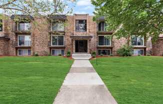 exterior view of a brick apartment building with green grass and a sidewalk