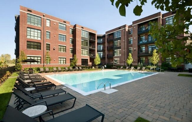 a swimming pool with chaise lounge chairs in front of an apartment building  at The Sheffield Englewood, Englewood, NJ, 07631