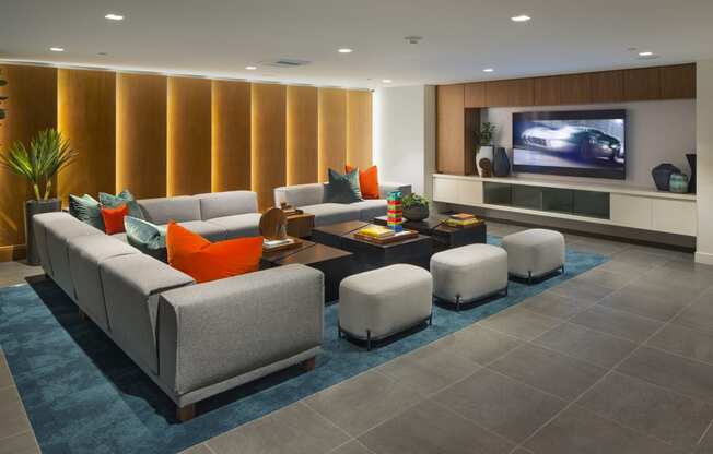 Studio Apartments in Woodland Hills, CA - The Q Variel - Media Room with Large Comfortable Couches, Wooden Tables Equipped with Books and Games, a TV, and Modern Décor