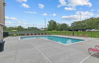 a swimming pool with chairs around it and a grassy field in the background