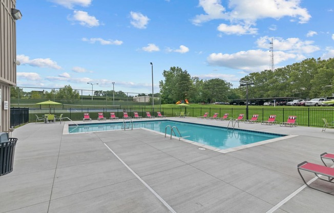 a swimming pool with chairs around it and a grassy field in the background