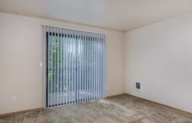 the spacious living room of an apartment with a large window and a sliding glass door