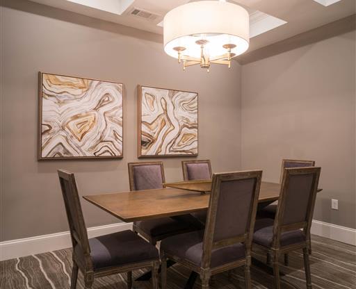 A dining room with a wooden table, upholstered chairs, and abstract wall art.