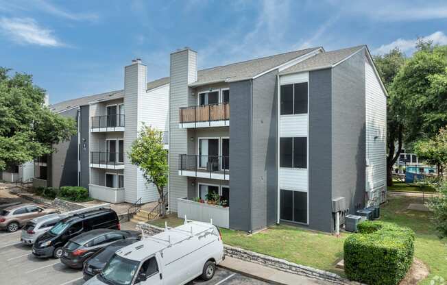 an image of an apartment building with cars parked in a parking lot