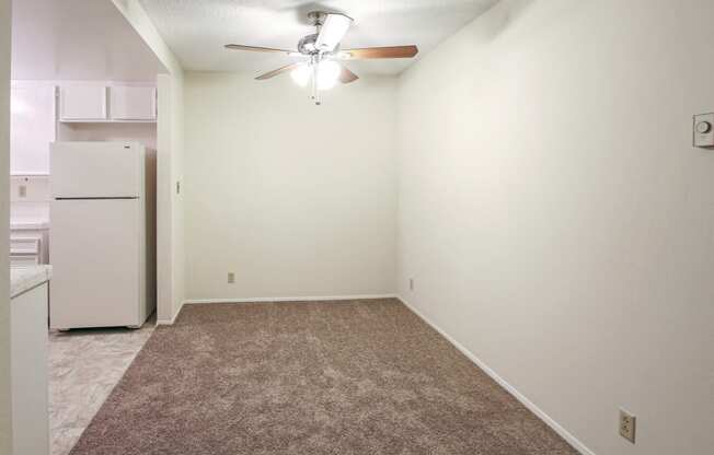 an empty room with a white refrigerator and a ceiling fan