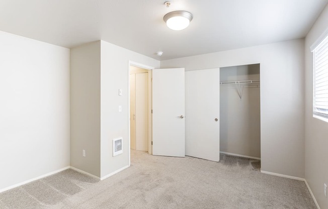 an empty bedroom with a closet and a window and beige carpet at Sitka Heights in Fife
