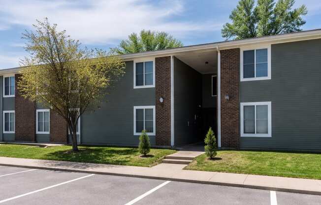 A grey apartment building with a parking lot in front.