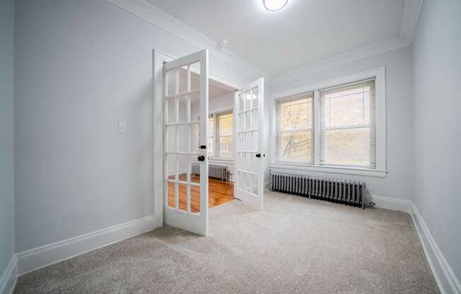 A room with a white door and a window with a radiator under the window.
