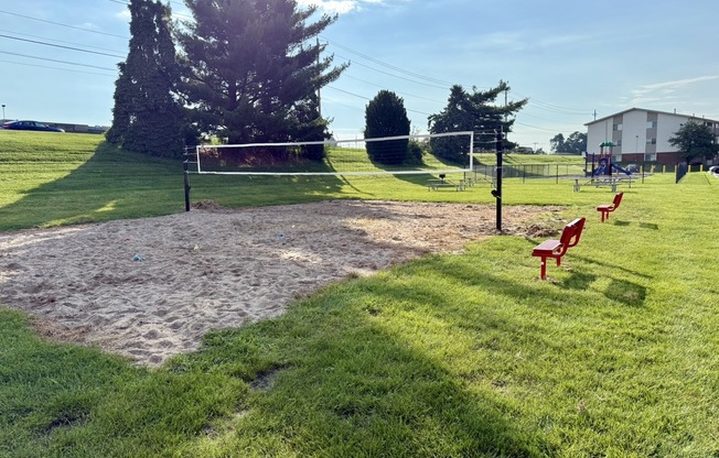 A sandy area with a volleyball net and red chairs.