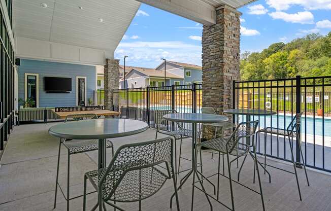 a patio with tables and chairs with an outdoor TV and a pool in the background