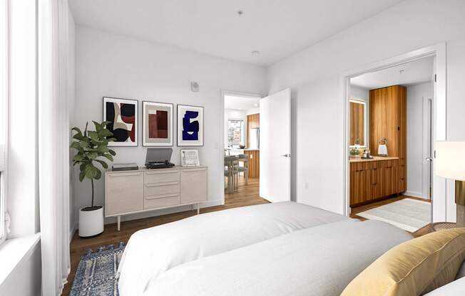 A white bedroom with a bed in the foreground and a desk with a laptop and a plant on it.