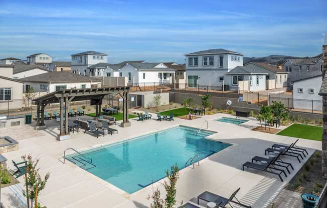 A large swimming pool surrounded by a patio with lounge chairs and a pavilion.