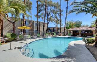 A pool surrounded by palm trees and a yellow umbrella.