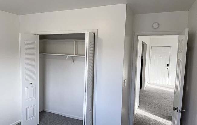 A bedroom with a white closet with a door open to a hallway at Waverly Park Apartments, Lansing