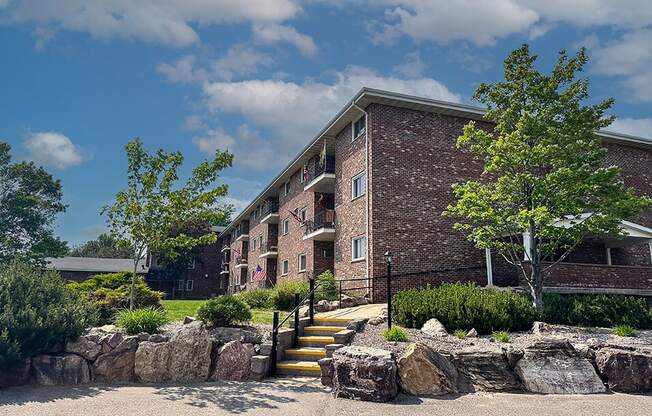 a brick apartment building with a stone retaining wall and landscaping