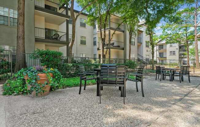 An al fresco dining patio with a table and chairs surrounded by lush trees at Jefferson Place Apartments in Irving, TX