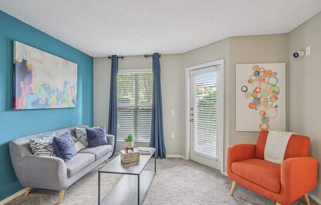 A living room with a grey couch, a red chair, and a glass coffee table at The Falls Apartments in Raleigh NC
