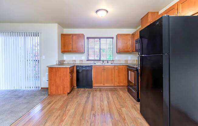 A black refrigerator is in the corner of a kitchen with wooden floors and cabinets.