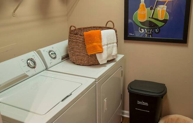 A laundry room with a washer and dryer, a basket on top of the dryer, and a poster on the wall.