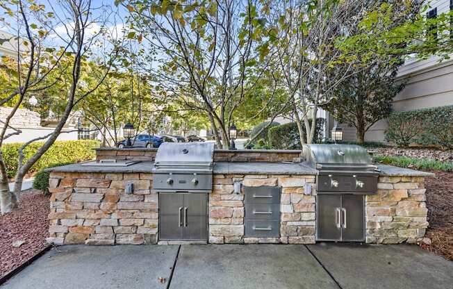 a stone barbecue area with two stainless steel appliances on the sidewalk