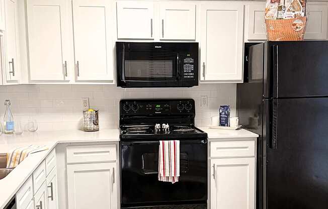 A black oven and refrigerator in a kitchen with white cabinets.