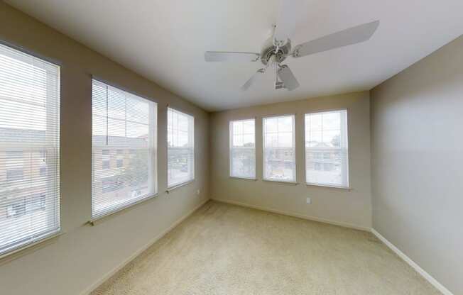 an empty living room with windows and a ceiling fan