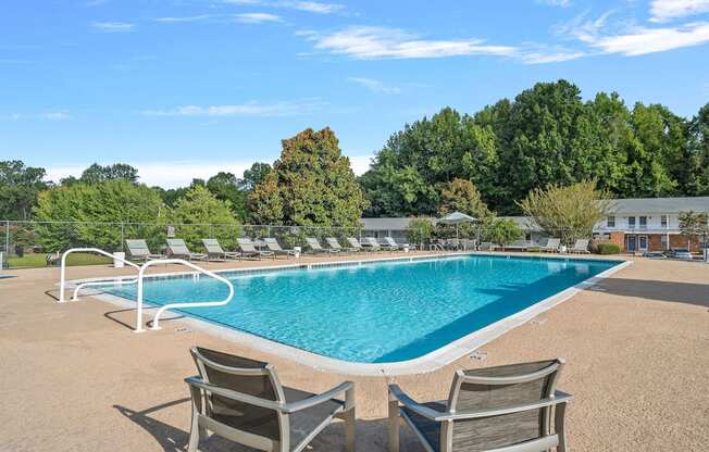 a swimming pool with chairs around it and trees in the background