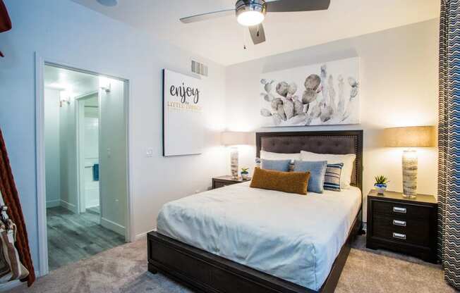 A bedroom with a bed, nightstand, and a wall art that says "enjoy".