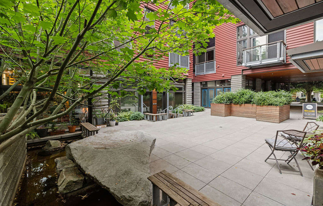 A patio with a bench and a tree in front of a building.