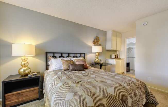 Model home bedroom with larger bed, side tables with decorative wall art. There is plush carpeting in the bedroom and built-in storage cabinets in the corner. 