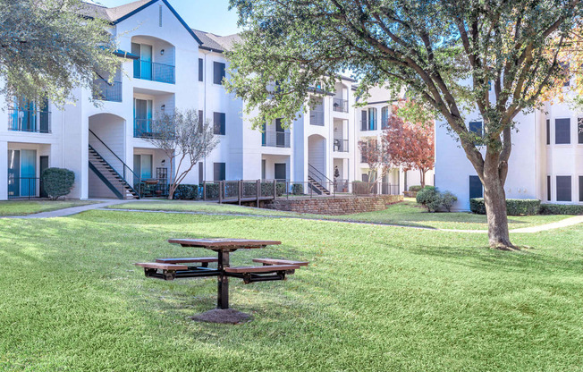 a picnic table sits in the grass in front of an apartment building