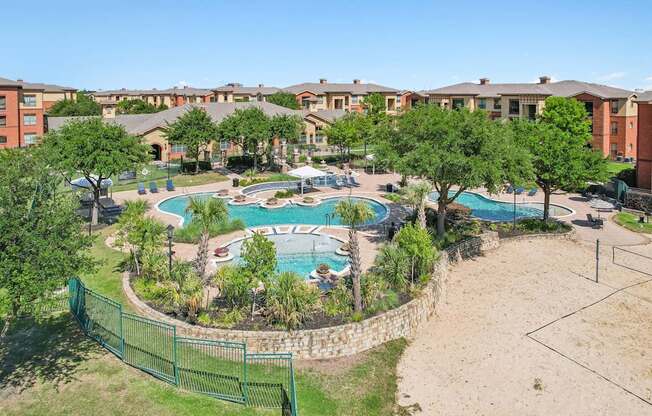 A large swimming pool surrounded by a fence and trees in a residential area.